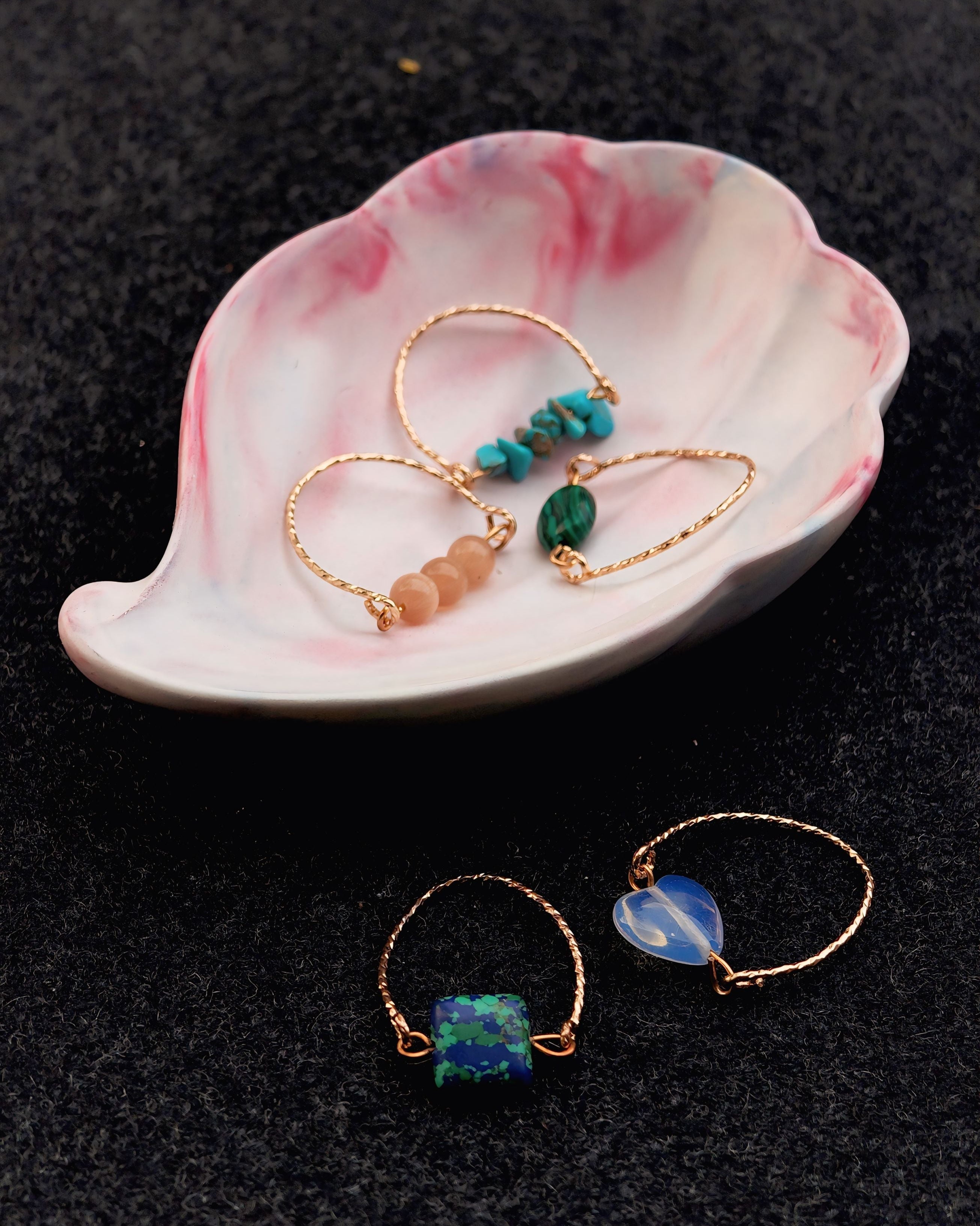 Jewelry set with gold and gemstone earrings on a pink and white ceramic dish against a black background.