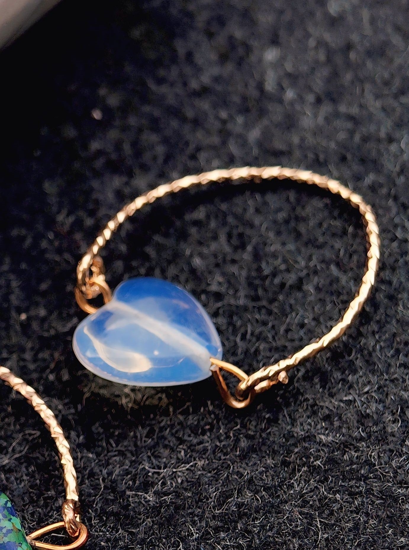 Gold bracelet with a heart-shaped blue stone on a dark textured background