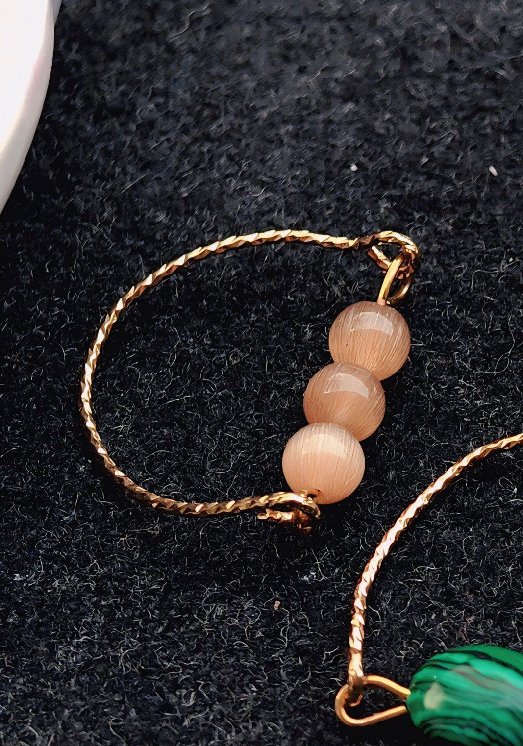 Ring with pink beads and gold braided strap on a dark background