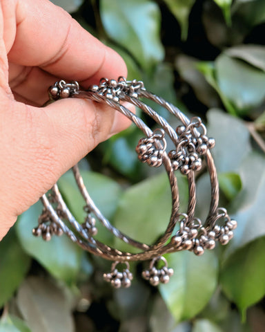 Silver bangles with bead details held by a hand against a green leafy background