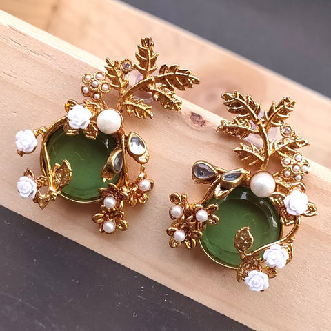 Gold and green earrings with leaf designs on a wooden surface