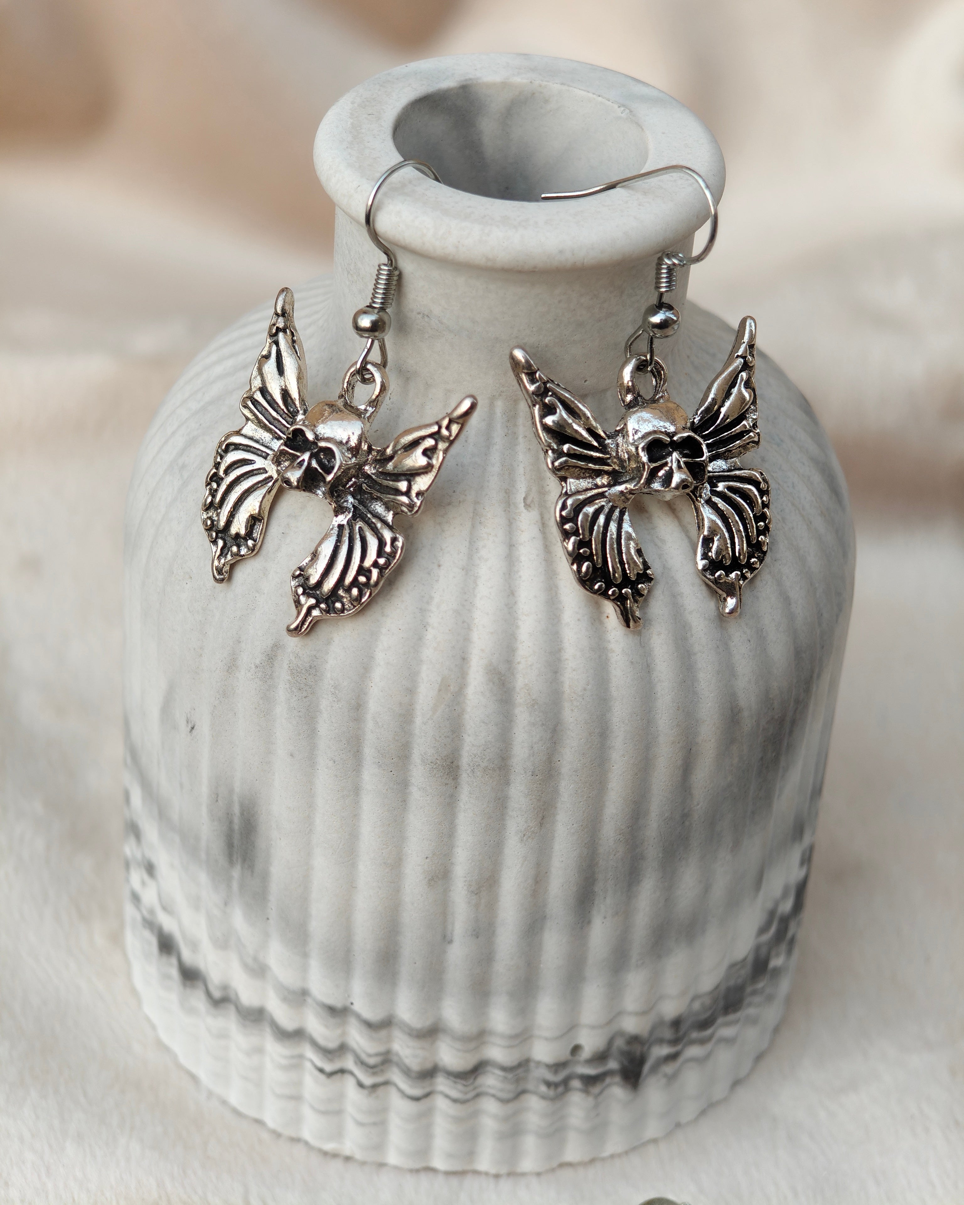Midnight Grunge 5-Pair Silver Gothic Earring Set on a marble tray, featuring textured snake hoops, sword dangles, skull butterflies, spiders, and witch knot earrings by Marjan Collections