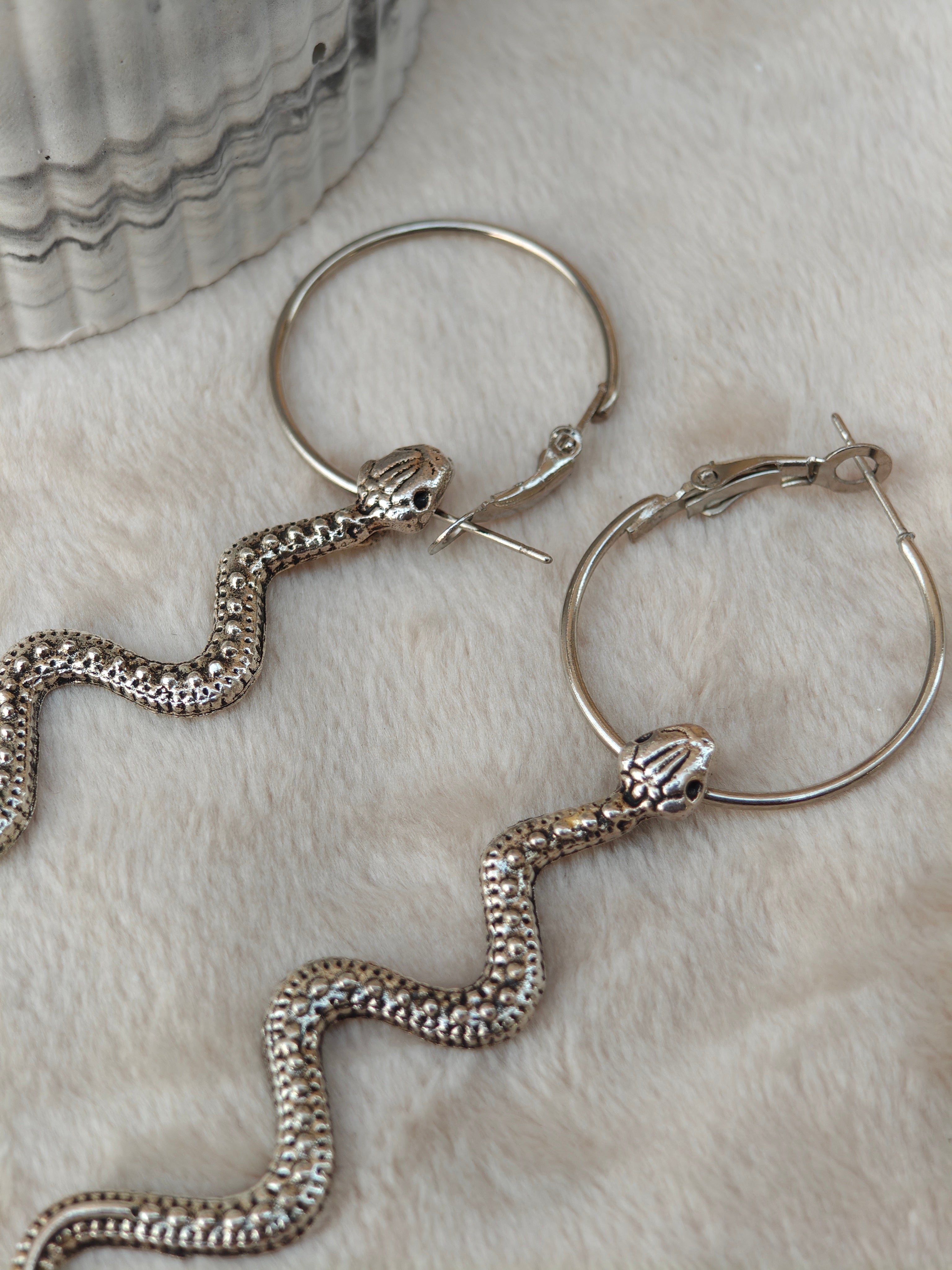 Midnight Grunge 5-Pair Silver Gothic Earring Set on a marble tray, featuring textured snake hoops, sword dangles, skull butterflies, spiders, and witch knot earrings by Marjan Collections