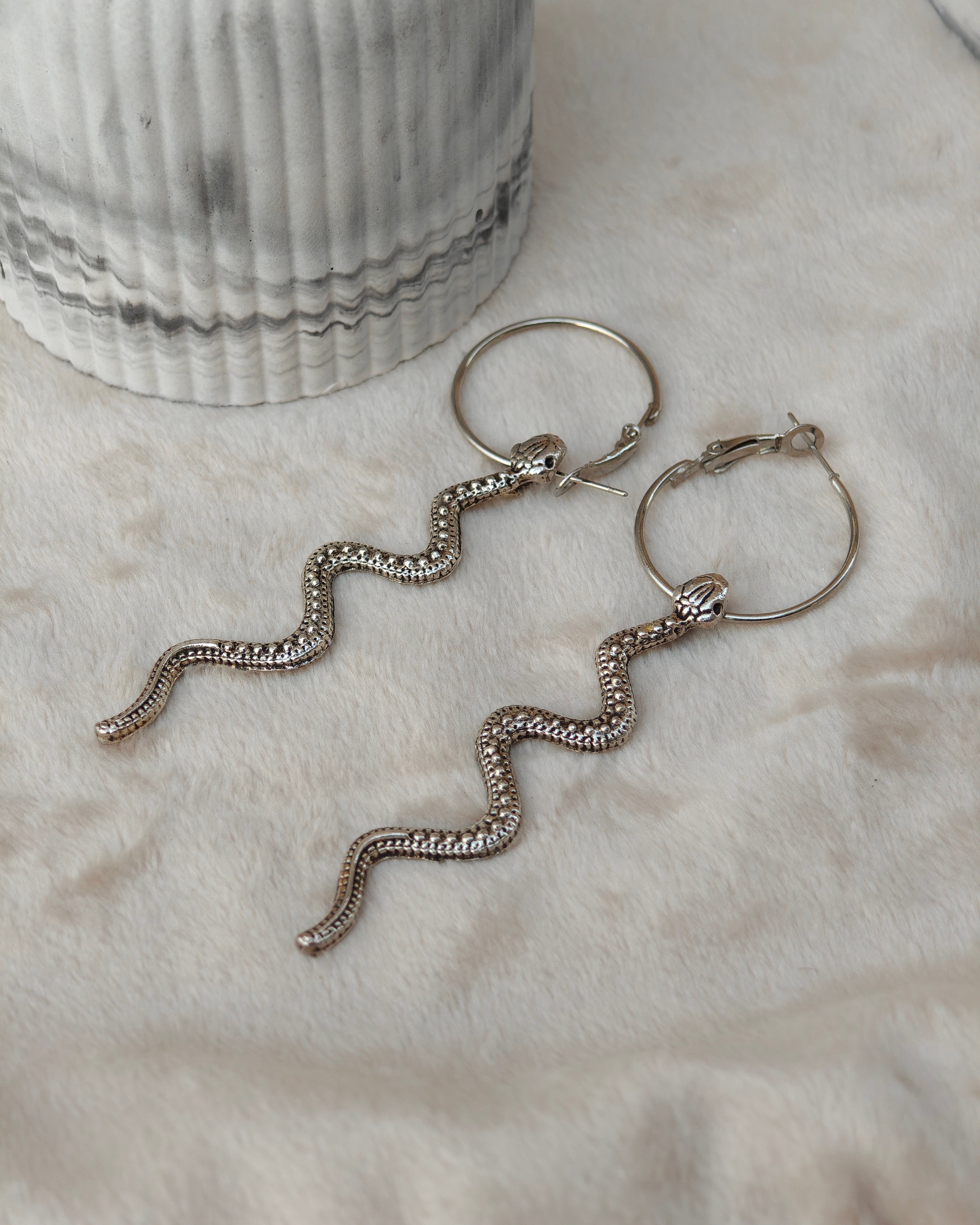 Midnight Grunge 5-Pair Silver Gothic Earring Set on a marble tray, featuring textured snake hoops, sword dangles, skull butterflies, spiders, and witch knot earrings by Marjan Collections