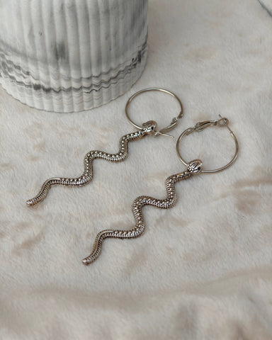 Midnight Grunge 5-Pair Silver Gothic Earring Set on a marble tray, featuring textured snake hoops, sword dangles, skull butterflies, spiders, and witch knot earrings by Marjan Collections