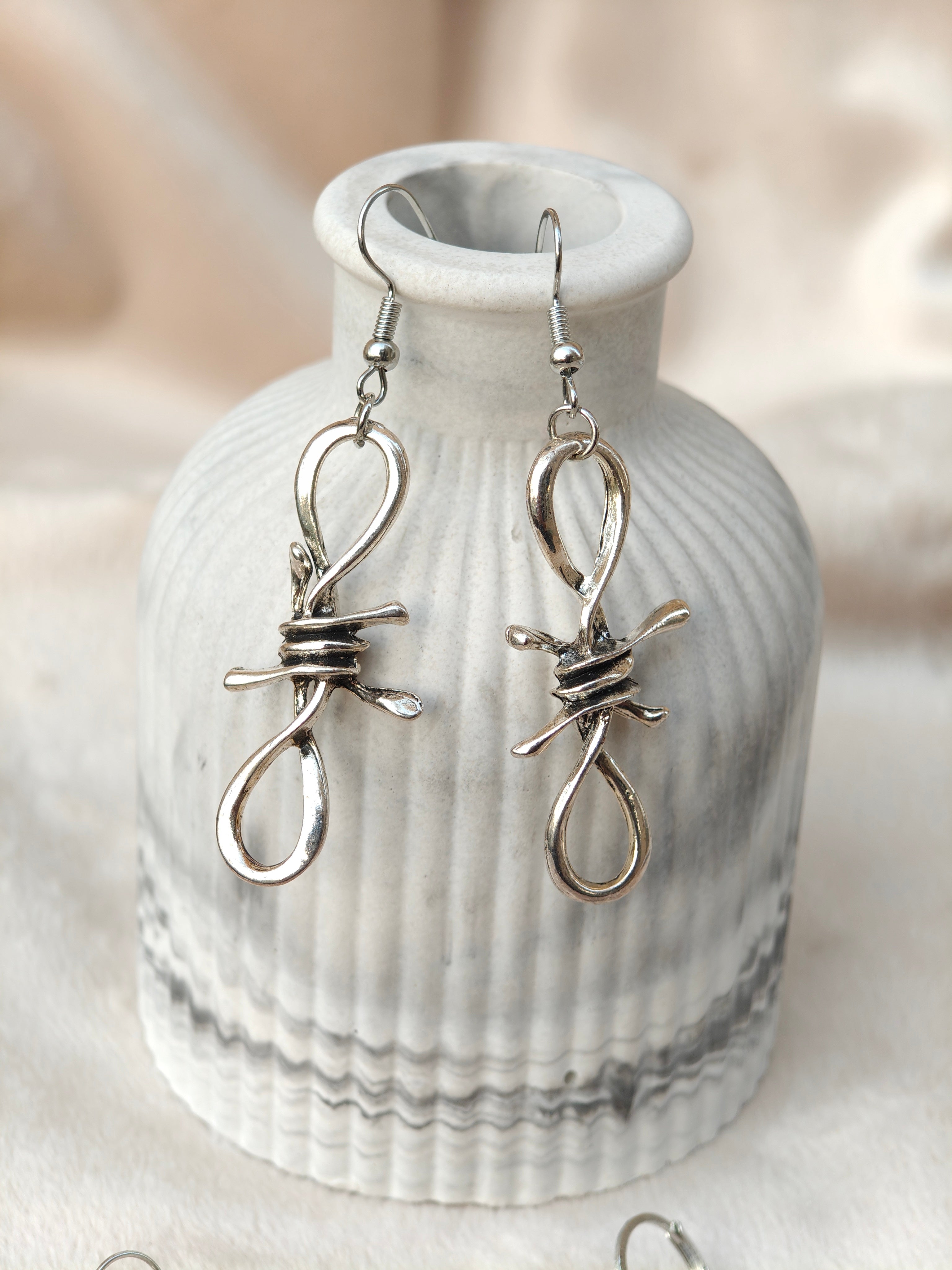 Midnight Grunge 5-Pair Silver Gothic Earring Set on a marble tray, featuring textured snake hoops, sword dangles, skull butterflies, spiders, and witch knot earrings by Marjan Collections