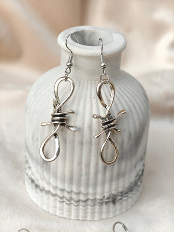 Midnight Grunge 5-Pair Silver Gothic Earring Set on a marble tray, featuring textured snake hoops, sword dangles, skull butterflies, spiders, and witch knot earrings by Marjan Collections