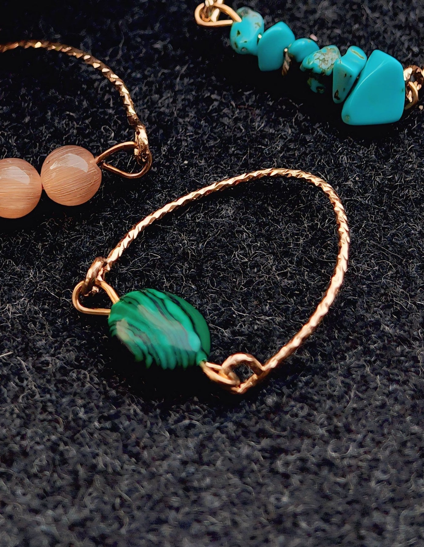 Close-up of gold bracelet with green stone on a dark textured surface