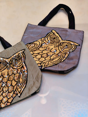 Two bags with owl designs made of sequins on a reflective surface.